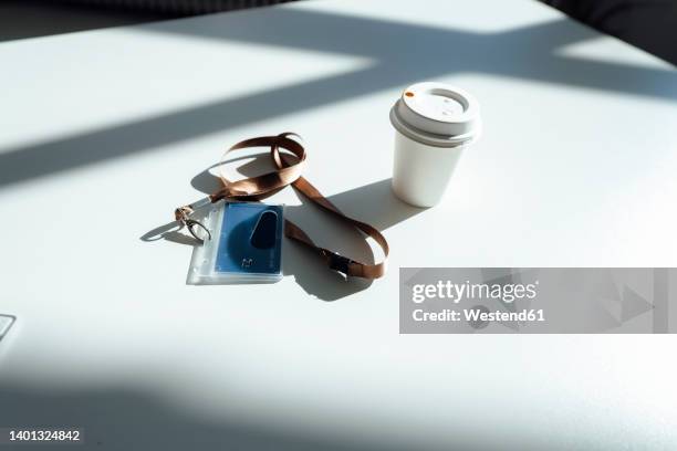 id card and disposable cup on white desk in sunlight - id card photos et images de collection