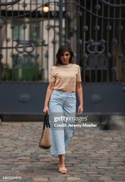 Anna Wolfers seen wearing a yellow/orange striped shirt, a light blue wide leg jeans with daisy print, a bast basket shopper bag and light orange...