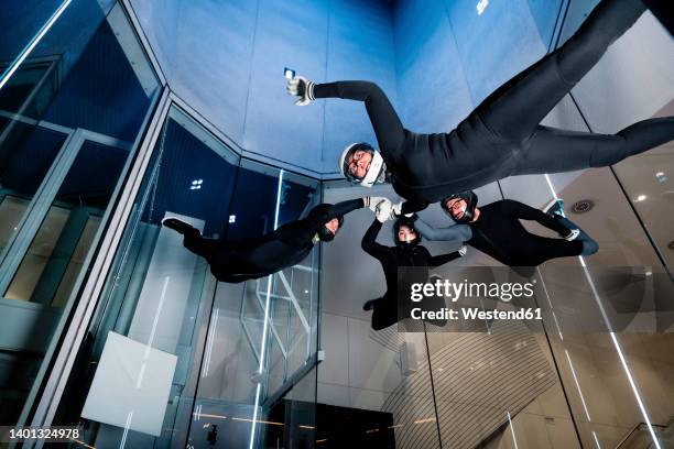 athletes holding each others hands flying in wind tunnel - indoor skydive stock pictures, royalty-free photos & images