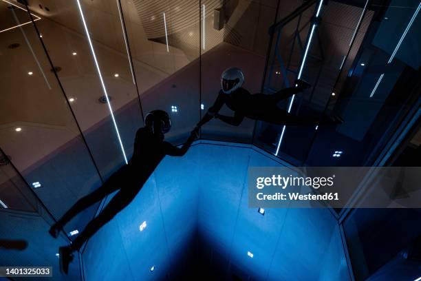 athletes holding each others hands flying in illuminated wind tunnel - indoor skydive stockfoto's en -beelden