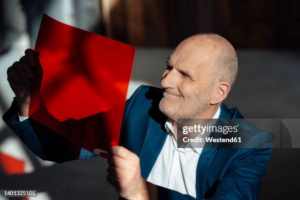 smiling businessman looking at red cellophane in office - celofán fotografías e imágenes de stock