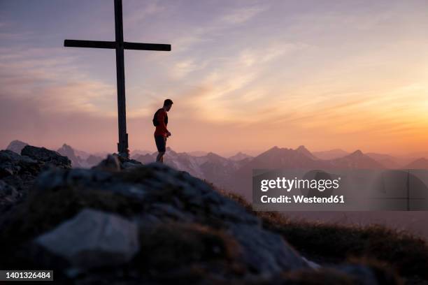 hiker standing by summit cross on mountain - gipfelkreuz stock-fotos und bilder