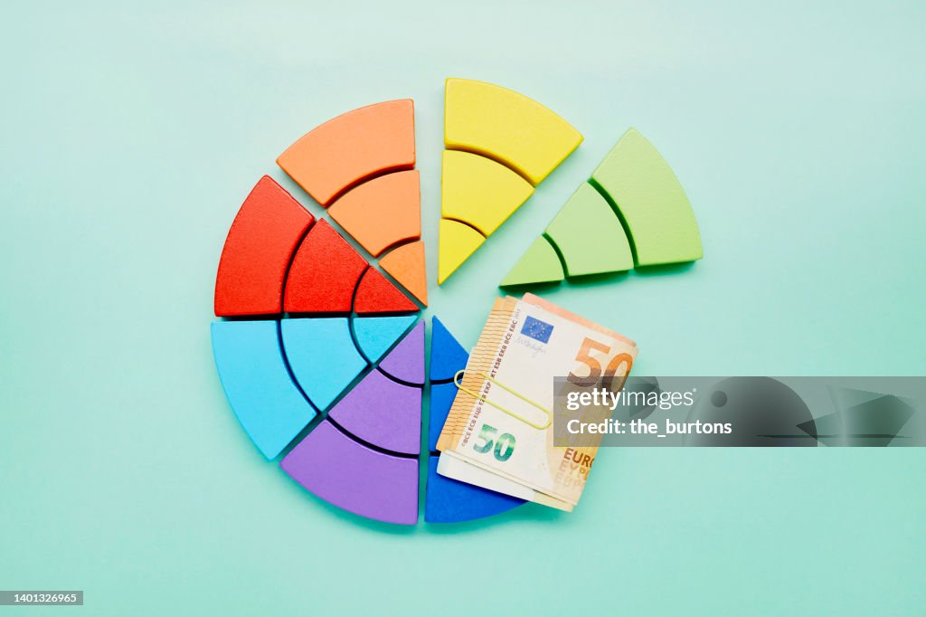High angle view of pie chart made of colorful building blocks and bunch of Euro banknotes on turquoise background