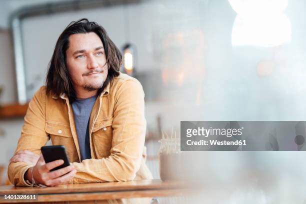 smiling man with mobile phone leaning on table at cafe - un seul homme d'âge moyen photos et images de collection