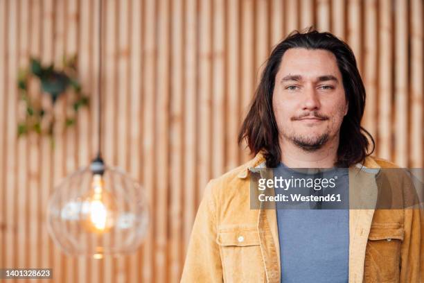hipster man with long hair standing in front of wall - one mid adult man only stock pictures, royalty-free photos & images