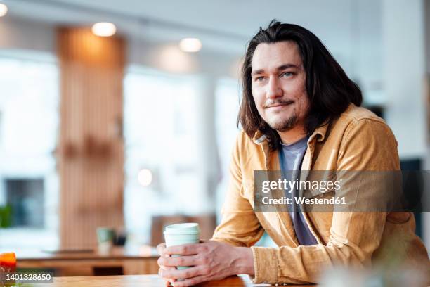 smiling hipster man with coffee cup leaning on table at coffee shop - einzelner mann über 30 stock-fotos und bilder