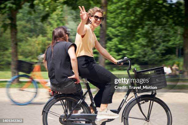 two women on a bicycle in urban park on a summer day, vondelpark, amsterdam - amsterdam cycling stock pictures, royalty-free photos & images