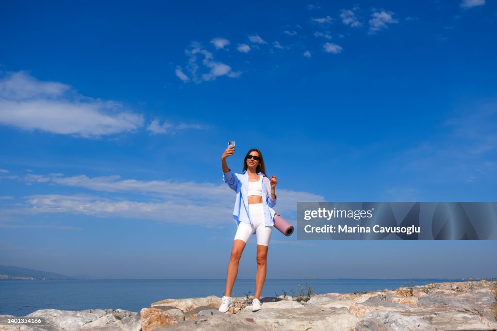 Young woman in sport outfit making selfie at the sea.