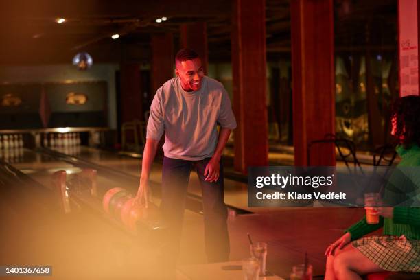 smiling man picking ball by female friend - bowlingbahn stock-fotos und bilder