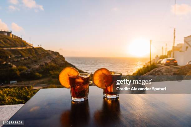 two glasses with cocktails at the table by the ocean during sunset - azenhas do mar stockfoto's en -beelden