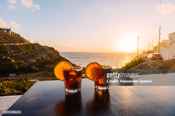 two glasses with cocktails at the table by the ocean during sunset - azenhas do mar imagens e fotografias de stock