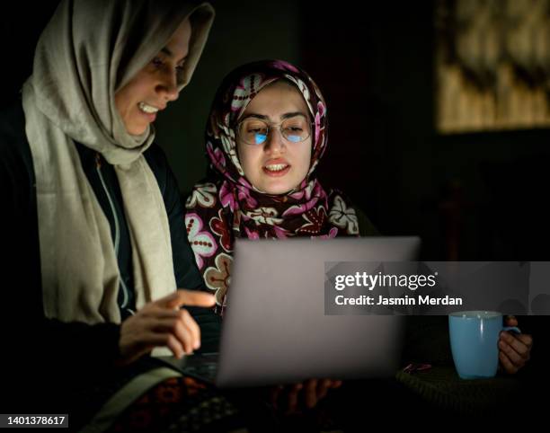 two arabic women in front of laptop - dark room foto e immagini stock