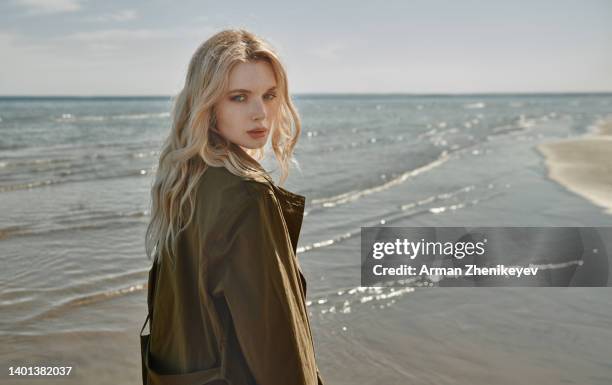 beautiful blond woman outdoors wearing coats next to the ocean - wavy hair stock pictures, royalty-free photos & images