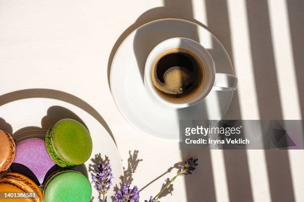 aromatic morning coffee in a white porcelain cup and cut lavender flowers, plate with french colorful macaroons, shadows on white  color background. - macaroon stock pictures, royalty-free photos & images