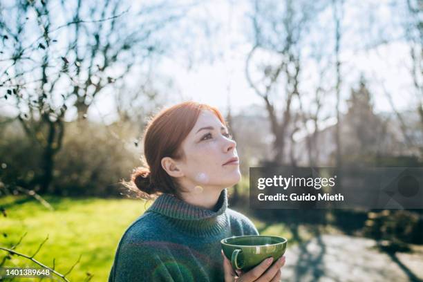 thoughtful looking redhead woman drinking hot tea outdoor. - hot white woman stock-fotos und bilder