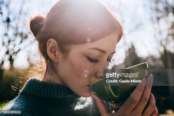 woman with red hair drinking tea outdoor. - infuso foto e immagini stock