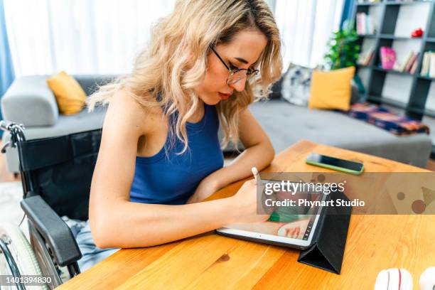 mujer de negocios discapacitada sentada en silla de ruedas trabajando con tableta digital en el lugar de trabajo - arab businesswoman with books fotografías e imágenes de stock