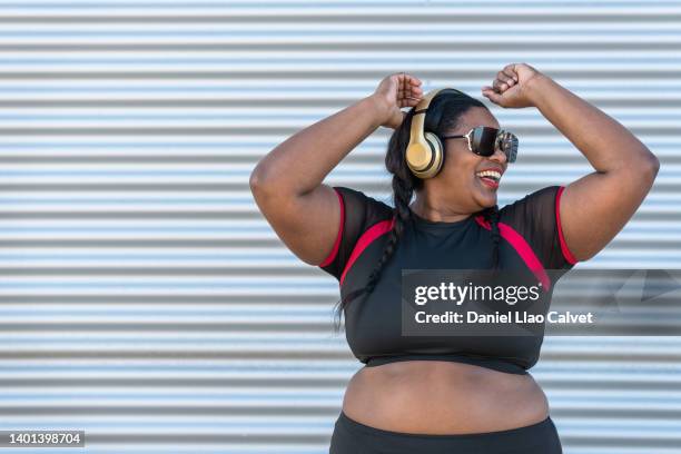 woman listening to music while dancing happily against a closed metal shutter - fat woman dancing stockfoto's en -beelden