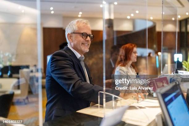 mature business traveler checking in at hotel reception - hotel opening party stock pictures, royalty-free photos & images
