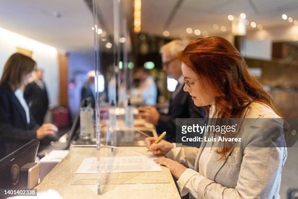 businesswoman checking in at the hotel reception - woman filling out paperwork stockfoto's en -beelden