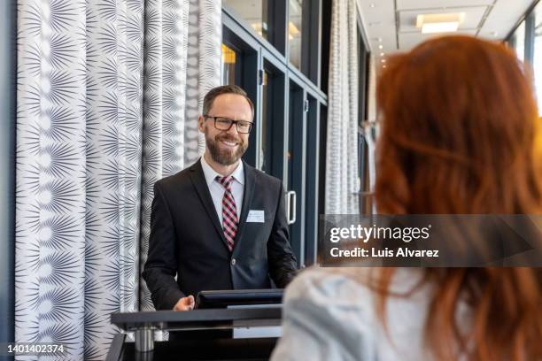 receptionist assisting a businesswoman at hotel reception desk - reception hotel photos et images de collection