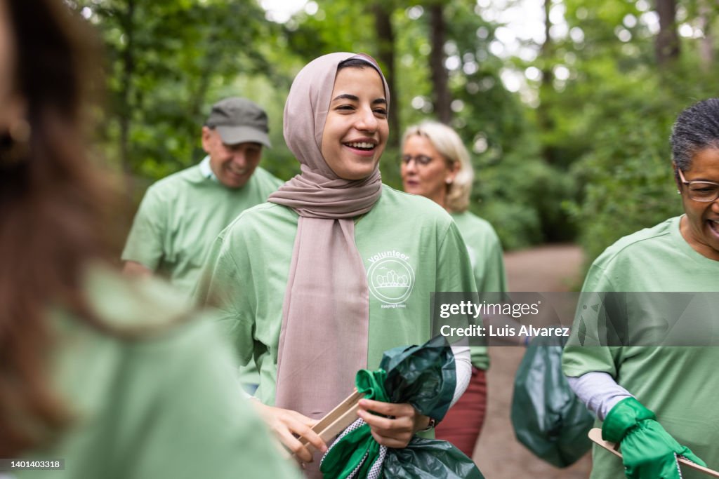 Muslim woman with volunteers walking through nature collecting garbage