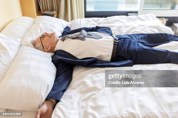 tired businessman lying on hotel room bed - letto matrimoniale foto e immagini stock