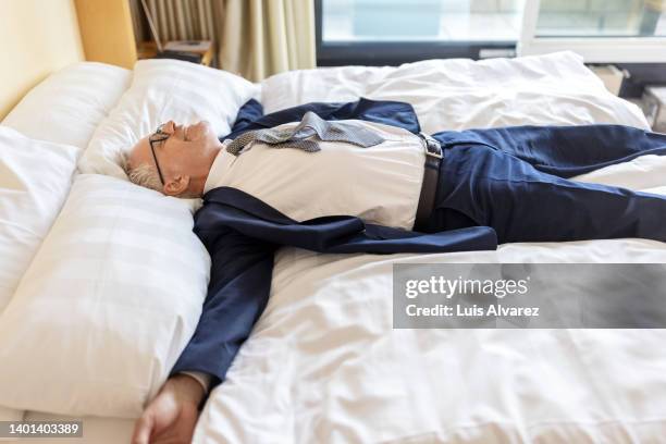 tired businessman lying on hotel room bed - man sleeping on bed stockfoto's en -beelden