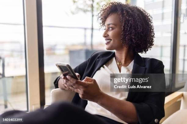 happy african woman sitting in hotel room with her mobile phone - hotel room work stock-fotos und bilder