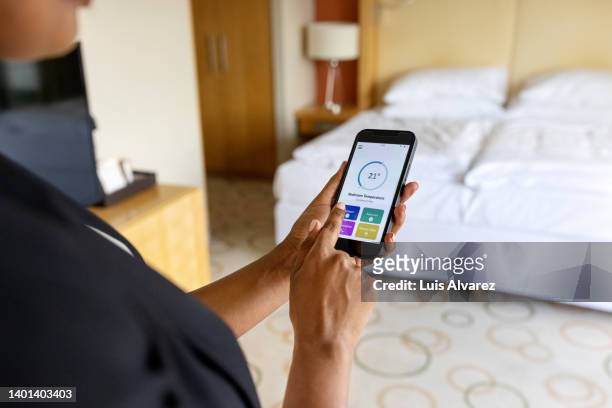close-up view of a woman adjusting her hotel room air conditioner with a smart phone app - ora del giorno foto e immagini stock