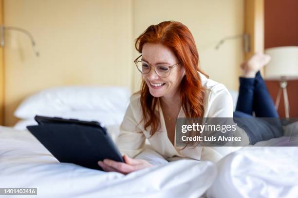 businesswoman lying on hotel room bed talking on a video call using her tablet - barefoot redhead ストックフォトと画像