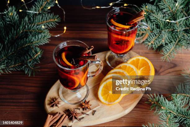 two glasses of christmas mulled wine with spices, orange, cinnamon, star anise, cloves stand on a wooden stand with green spruce branches. warm cozy winter and autumn drink. - punsch tasse stock-fotos und bilder