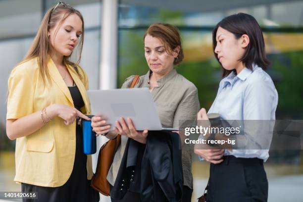 group of businesswomen checking laptop on the go on front of office building - reusable water bottle office stock pictures, royalty-free photos & images