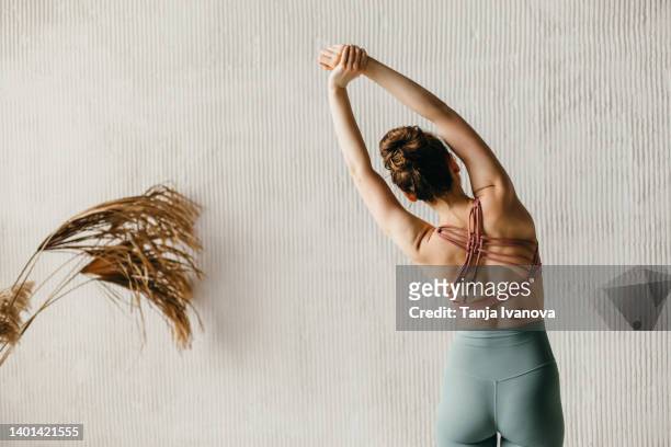 back view of young woman doing yoga against a gray wall. copy space - back stretch stockfoto's en -beelden
