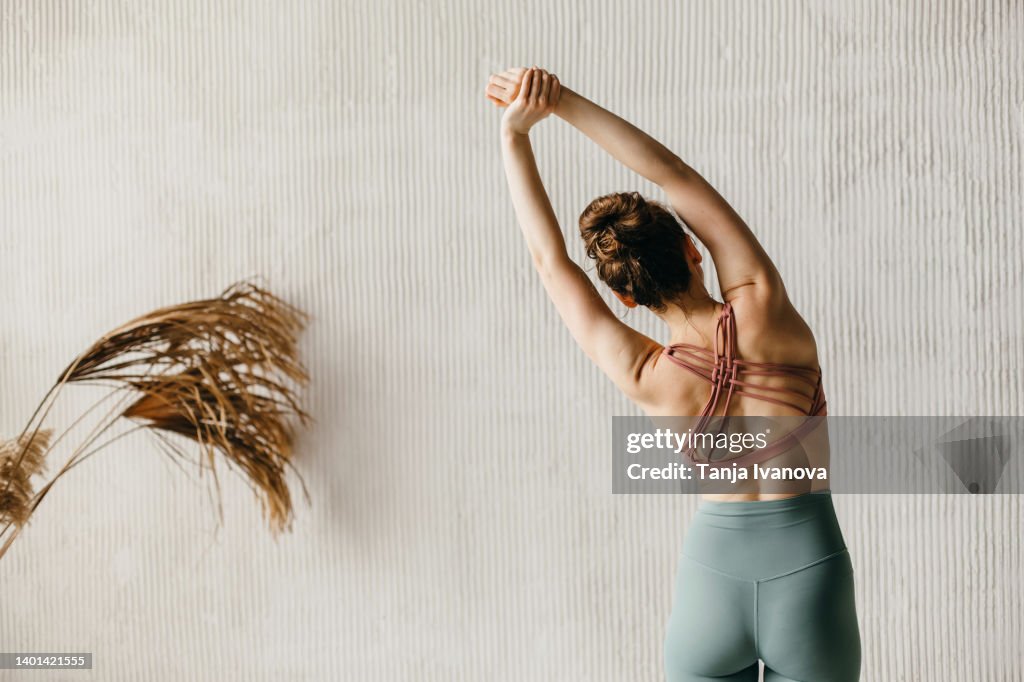 Back view of young woman doing yoga against a gray wall. Copy space