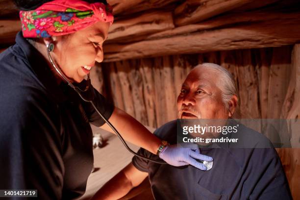 weibliche rettungssanitäterin notfallmedizinerin hört auf das herz und die lunge ihrer patientin, während sie patienten visitiert, die nach hause gebunden sind, um sicherzustellen, dass es ihnen gesundheitlich gut geht - indigenous american culture stock-fotos und bilder