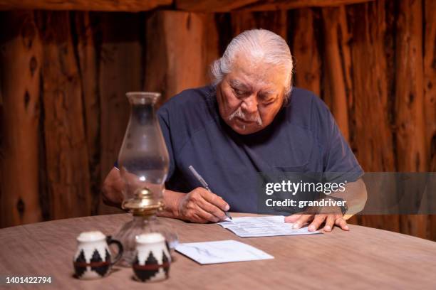 senior adult male sitting at the table in his hogan filling out his mail-in ballot for the upcoming election - indian politics and governance stockfoto's en -beelden