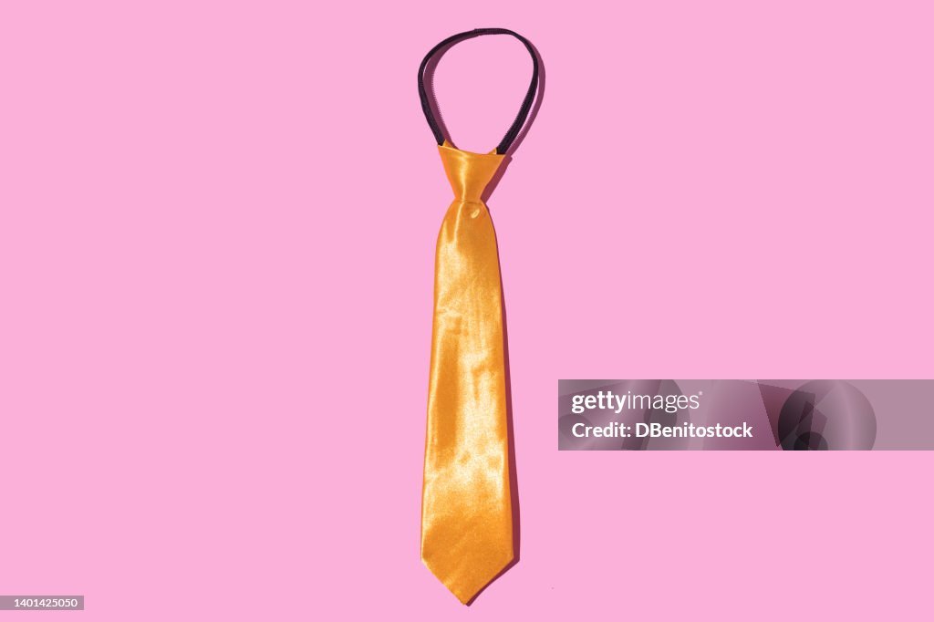 Gold yellow silk tie on pink background. Party, celebration,, elegance and costume concept.