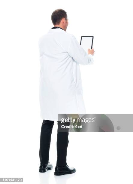 kaukasischer junger männlicher arzt, der vor weißem hintergrund im laborkittel und mit digitalem tablet steht - doctor lab coat stock-fotos und bilder