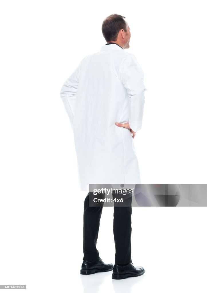 Caucasian young male doctor standing in front of white background wearing lab coat