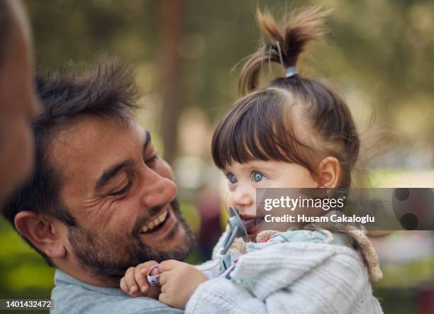 a cute little girl smiling with her pacifier in her mouth at the person who pranks her on her father's lap. - 1 year anniversary stock pictures, royalty-free photos & images