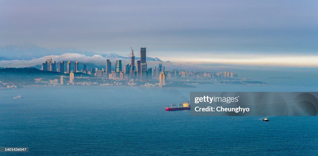 Drone Point View of Large Cargo Ship in front of Qingdao City Skyline in the Mist
