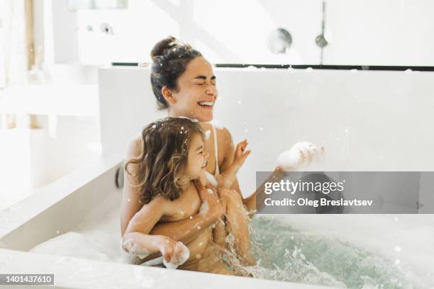 mother and cute baby daughter having fun and laughing in bath tub full of foam bubbles - woman bath bubbles stock-fotos und bilder