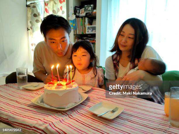 a family celebrating a birthday. - parents children blow candles asians foto e immagini stock