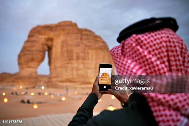 saudischer mann fotografiert elephant rock mit smartphone - desert elephant stock-fotos und bilder