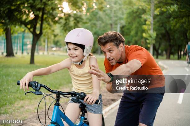 portrait of a cute girl riding a bike and her father helping her - girl bike stock pictures, royalty-free photos & images