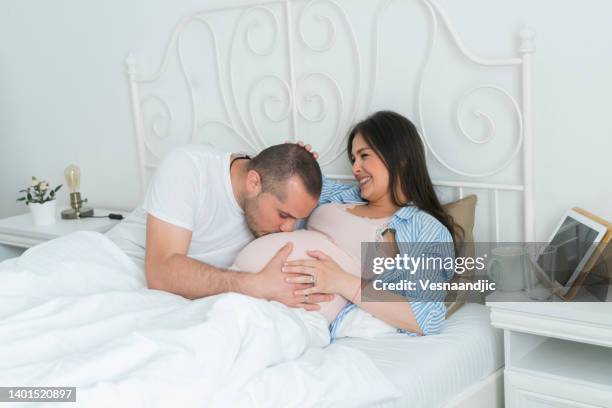 parents in bed, father kissing belly - belly kissing stockfoto's en -beelden