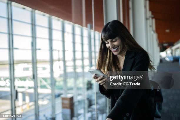 happy young woman using smartphone in an airport - candid forum 個照片及圖片檔