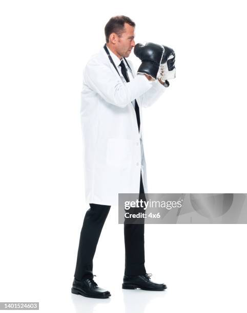 caucasian male doctor standing in front of white background wearing boxing glove - fighting stance stock pictures, royalty-free photos & images