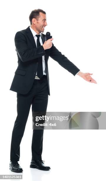 caucasian young male public speaker standing in front of white background wearing businesswear and holding microphone - presenter stockfoto's en -beelden